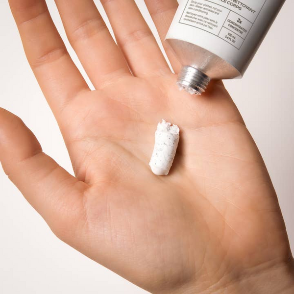 Hand holding a small amount of white cream with a tube above it on a light background