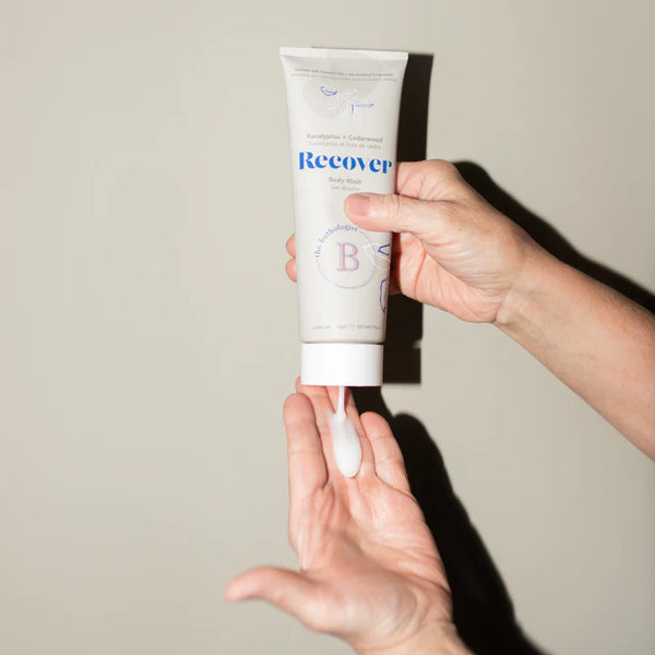 Hand holding a tube of 'Recover' body wash against a neutral background