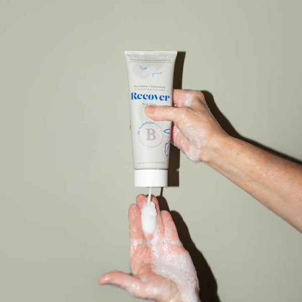Hand holding a tube of 'Recover' body wash against a plain background
