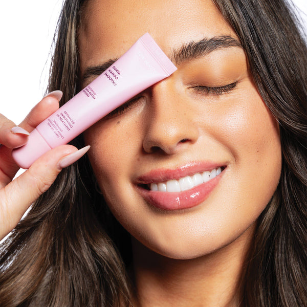 Woman applying pink lip gloss to her face with a white background