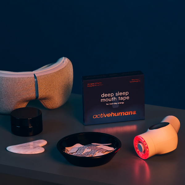 Product set including a sleep mask, mouth tape, and a small device on a dark surface with a dark background.