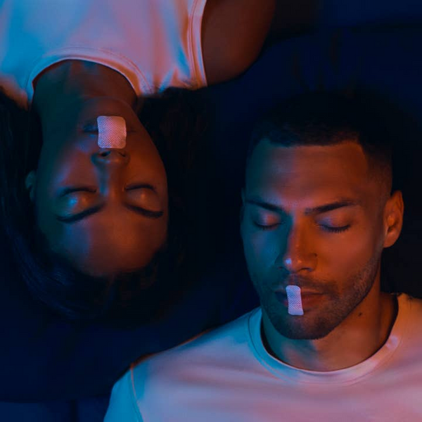 Two people lying down with bandages on their mouths in a dark setting