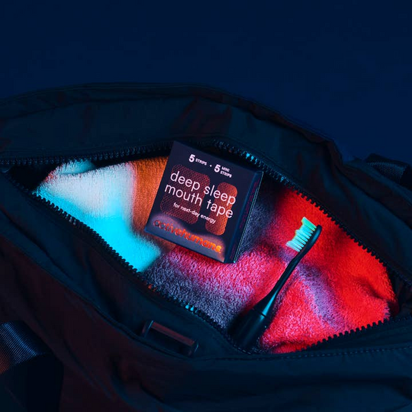Box of 'deep sleep mouth tape' on a towel with a toothbrush, inside an open bag.