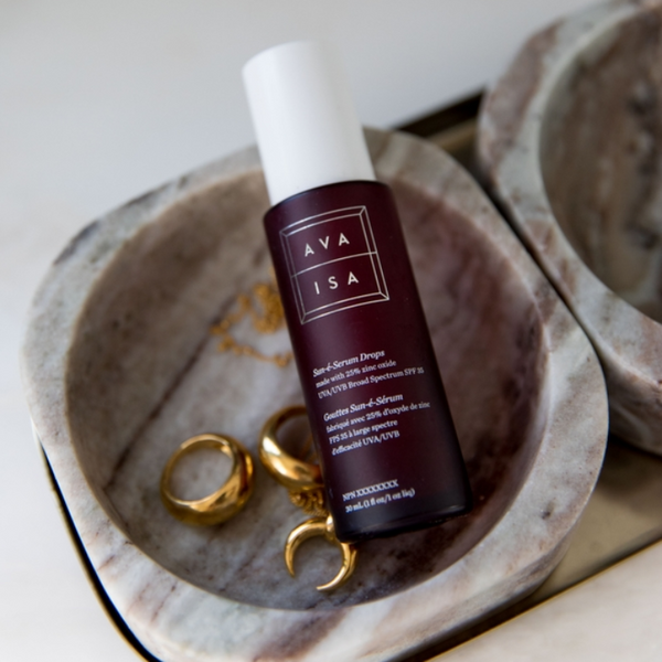 Ava Isa skincare bottle with gold earrings on a stone surface