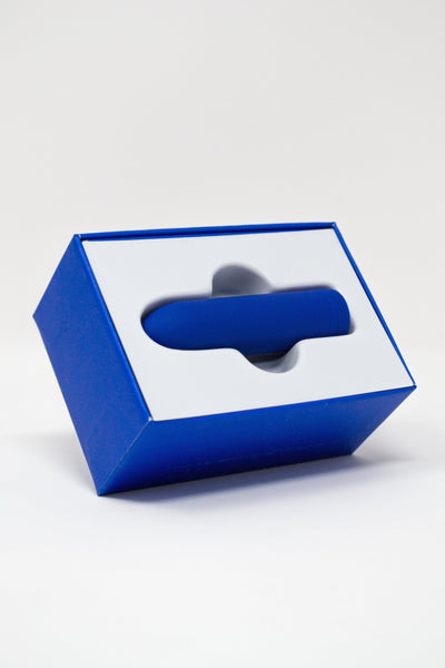Blue box with a white interior holding the Zee Bullet Vibrator by Dame on a light gray background