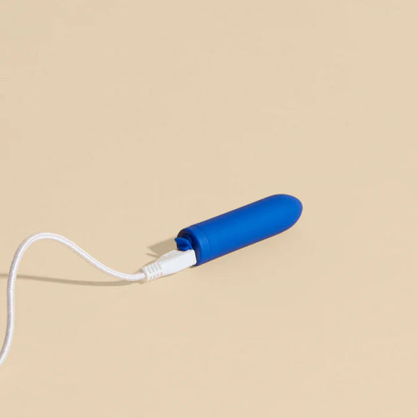 Blue Zee Bullet Vibrator with a white cord on a beige background