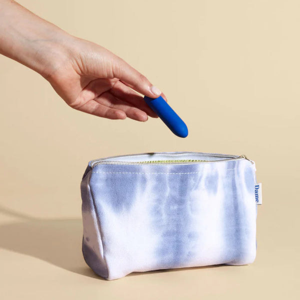 Hand holding a cobalt blue Zee Bullet Vibrator above a white pouch with a beige background
