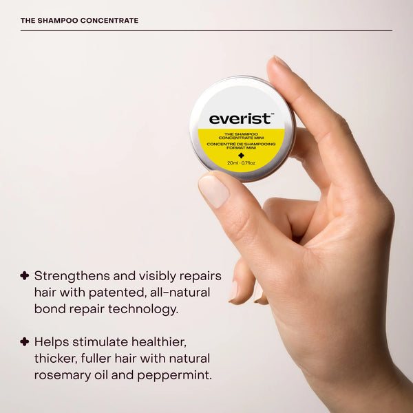 Hand holding a container of Everist shampoo concentrate travel tin with product details on a light background