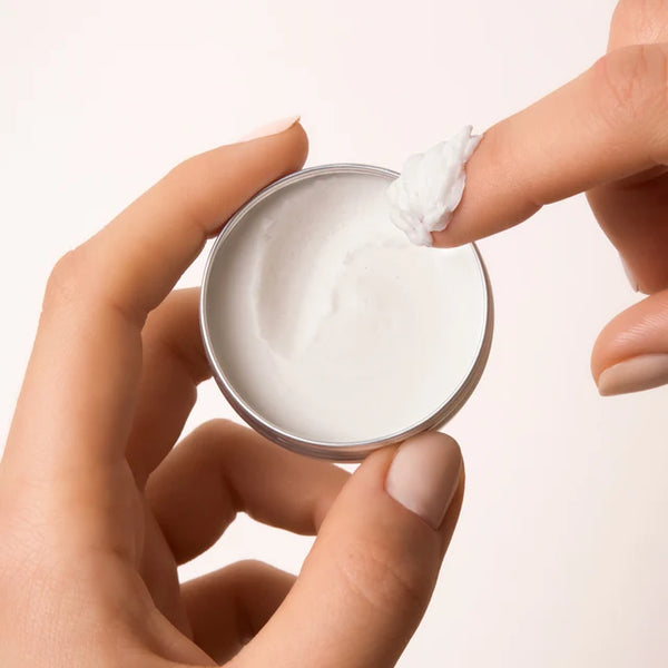 Hand scooping The Body Wash Concentrate from a small tin container on a light background