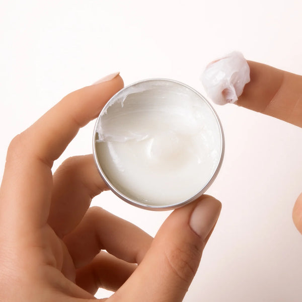 Hand holding a small container of The Deep Conditioning Concentrate with a blurred background