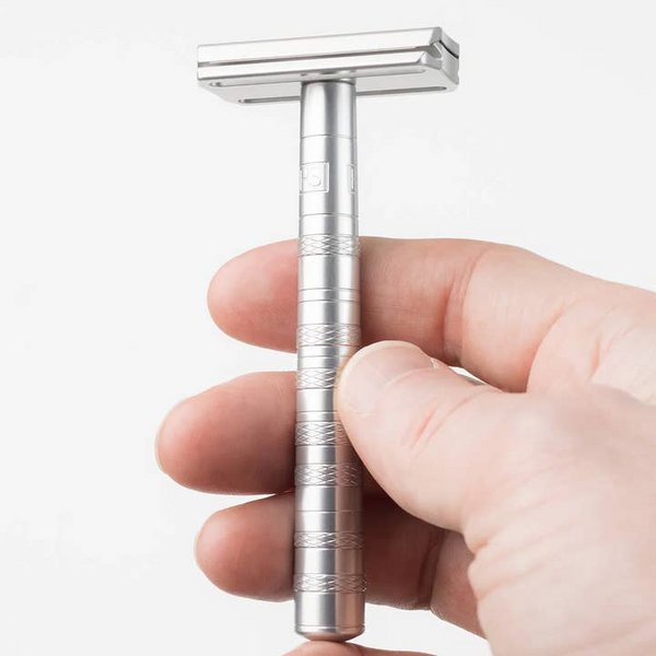 Silver safety razor held in a hand against a white background