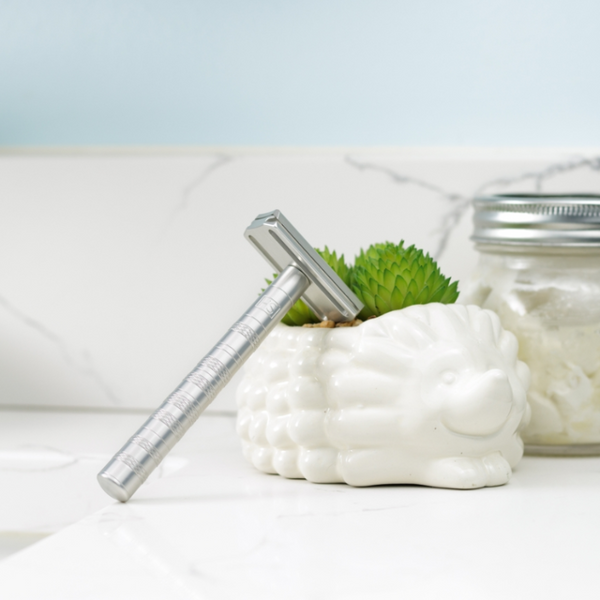 Shaving cream, razor, and jar on a white surface with a light blue background