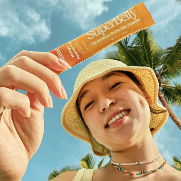 Person holding a Superbelly drink mix packet with palm trees and blue sky in the background