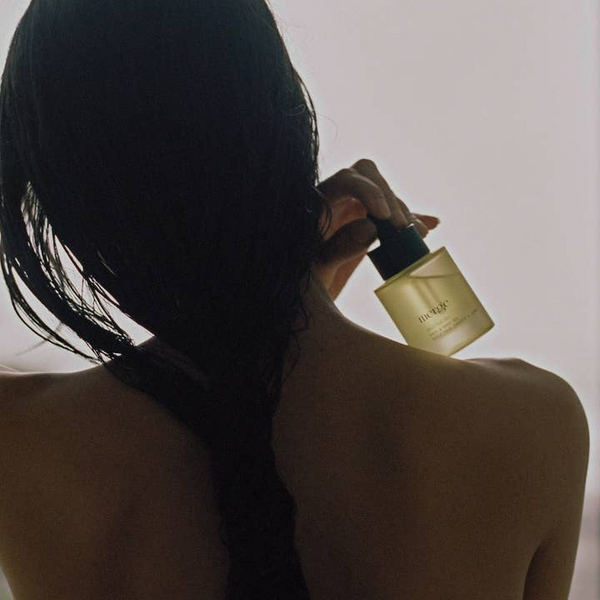 Person applying perfume to their shoulder with a neutral background