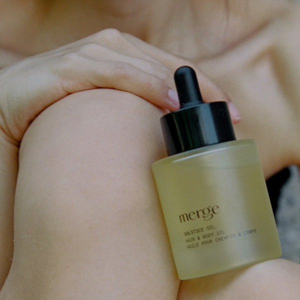 Bottle of 'merge' skincare product held by a person with blurred background