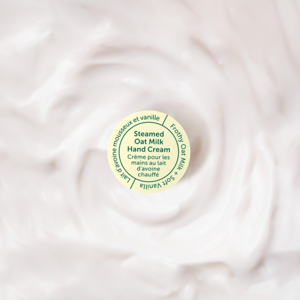 Round container of steamed oat milk cream on a swirling white background