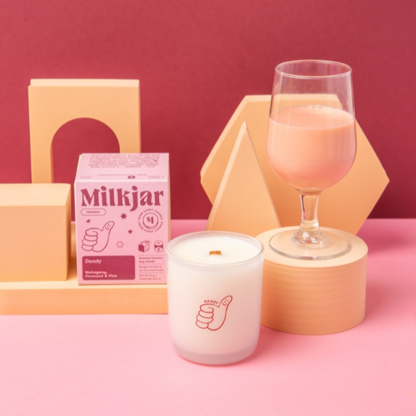 Milkjar product with a candle and glass on a pink background
