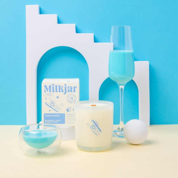 Milkjar product with a candle, glass, and decorative elements on a blue background