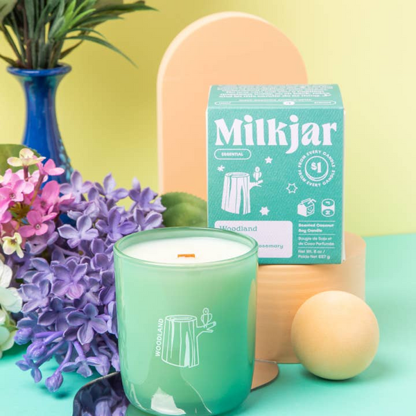 Green candle in a Milkjar container with a box, flowers, and decorative items on a colorful background