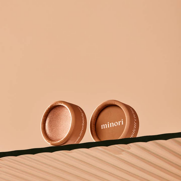 Two bronze-colored cosmetic containers with 'minori' branding on a beige background