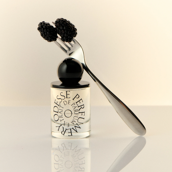 Perfume bottle with blackberries and a fork on a reflective surface