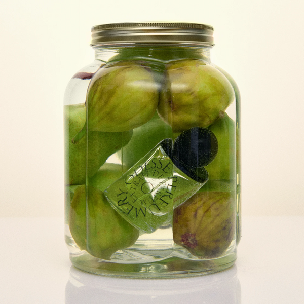 Glass jar filled with green figs on a white background