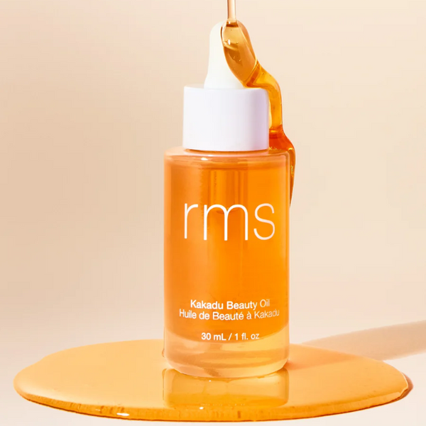 Orange bottle of rms Kakadu Beauty Oil with a droplet on a beige background