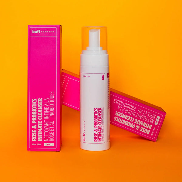 White bottle and pink boxes of Rose & Probiotics Intimate Cleanser by Buff Experts on an orange background