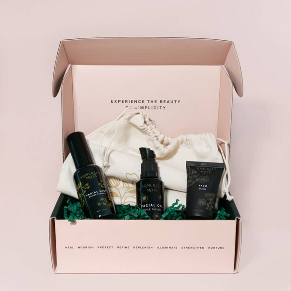 Skincare product set with bottles and a drawstring bag in a pink box on a light pink background. Somerset Moss