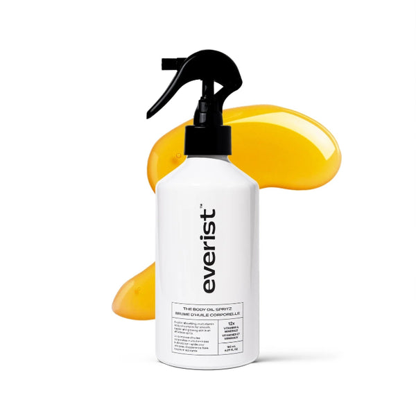 A white Everist spray bottle with a black trigger sprayer, shown against a white background with a glossy yellow smear behind it. The bottle label reads 'everist' and 'THE BODY OIL SPRAY'.