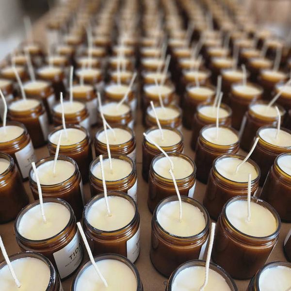 Row of brown glass jars with white candles on a cardboard surface