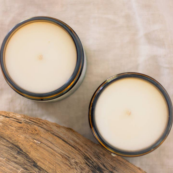 Two small candles in rustic containers on a wooden surface with a neutral background