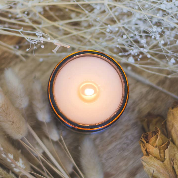 Candle with a warm glow surrounded by dried flowers on a wooden surface
