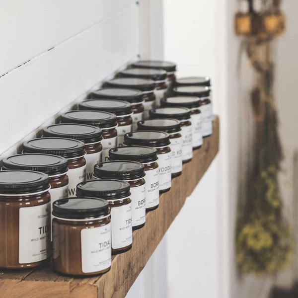 Row of jars with black lids on a wooden shelf against a white wall.