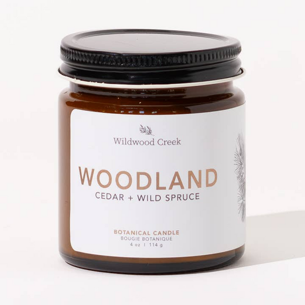 Candle jar labeled 'Woodland Cedar + Wild Spruce' by Wildwood Creek on a white background