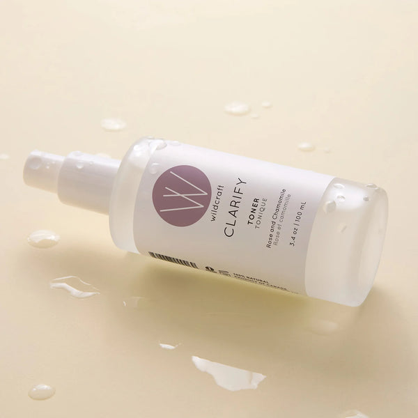 Wildcraft Clarify Toner in a frosted white spray bottle with water droplets, resting on a light beige surface with water droplets.