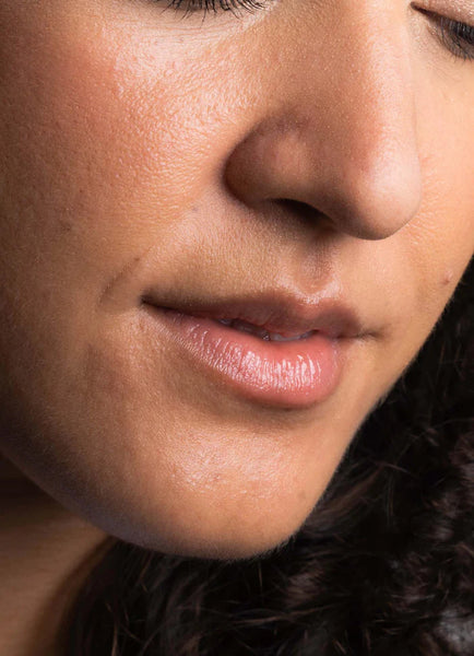 Close-up of a woman's face with a soft focus on her lips and skin wearing Good Gloss in colour Dream