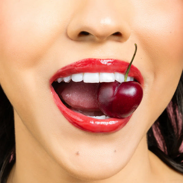Close-up of a woman's mouth with red lipstick holding a cherry.