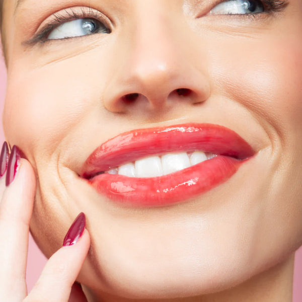 Close-up of a woman's face with a bright smile on a pink background