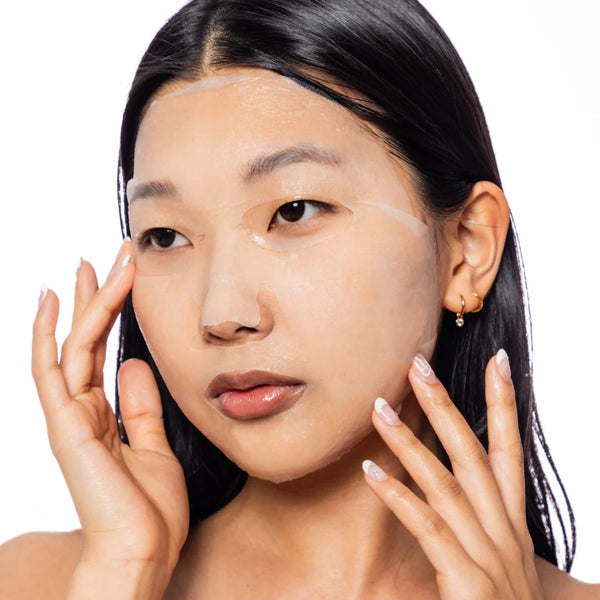 Woman with hands on face against a white background while wearing a biocellulose fask mask from ESW Beauty.